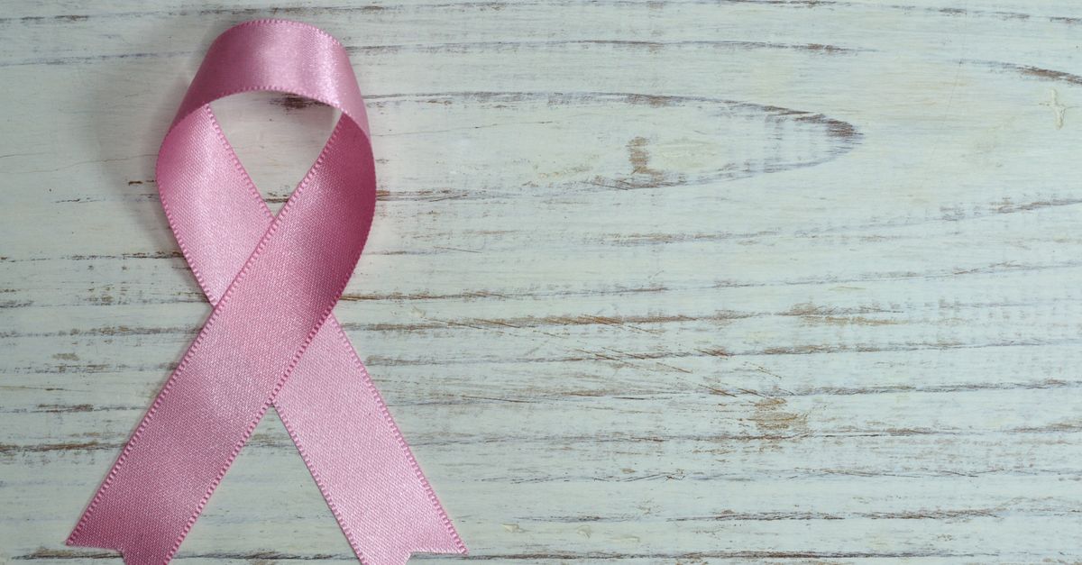 A pink ribbon symbolizing cancer awareness placed on a light wooden background.