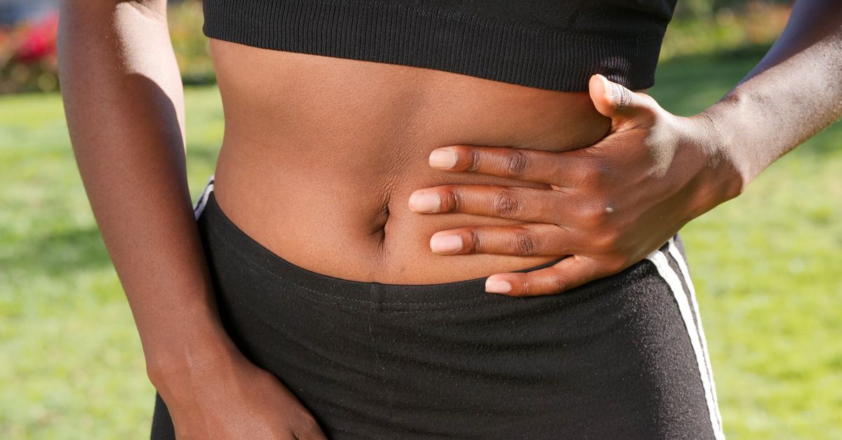 Close-up of a person holding their abdomen, indicating stomach discomfort, outdoors.